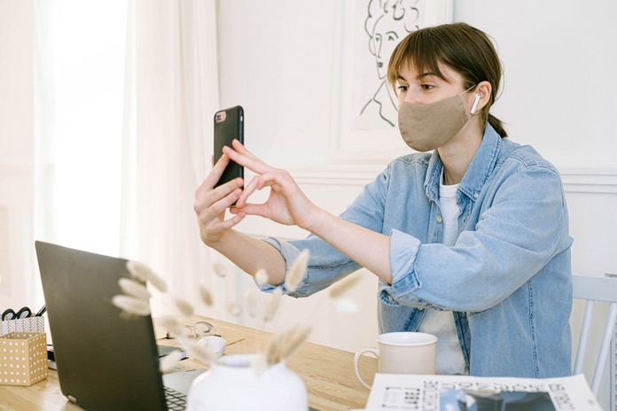 woman-wearing-facemask-in-front-of-laptop-making-selfie